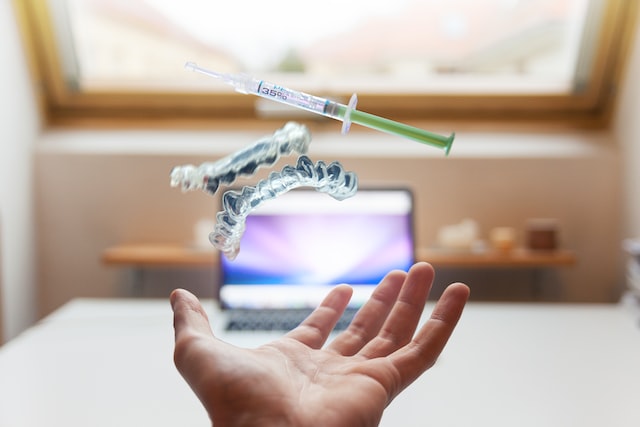 open hand with a laptop in front and floating dentures and syringe above it
